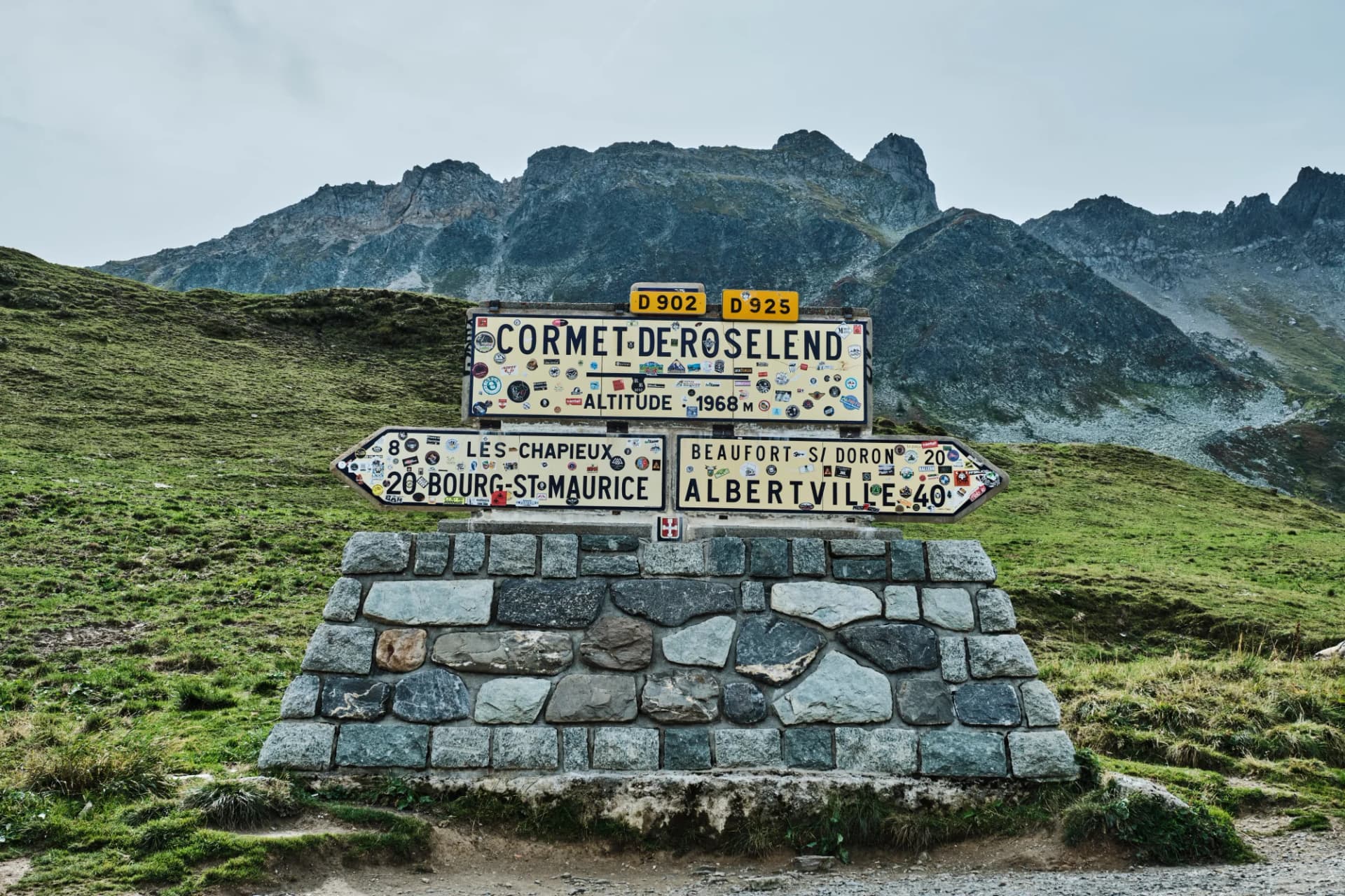 Cormet-de-Roselend altitude sign on stone base with mountains and green slopes.