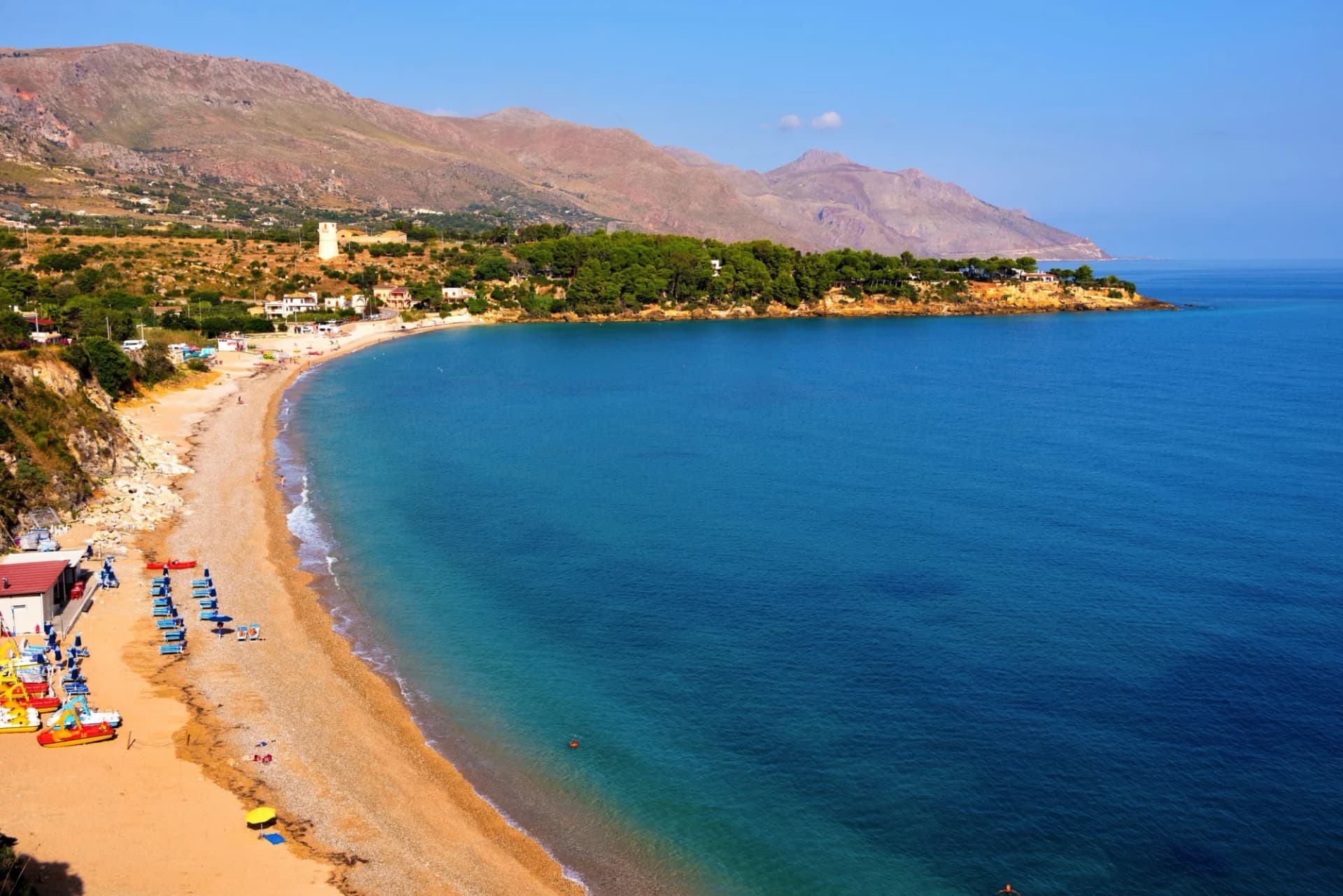Beach in Castellammare del Golfo, Italy, with turquoise sea and arid mountains.