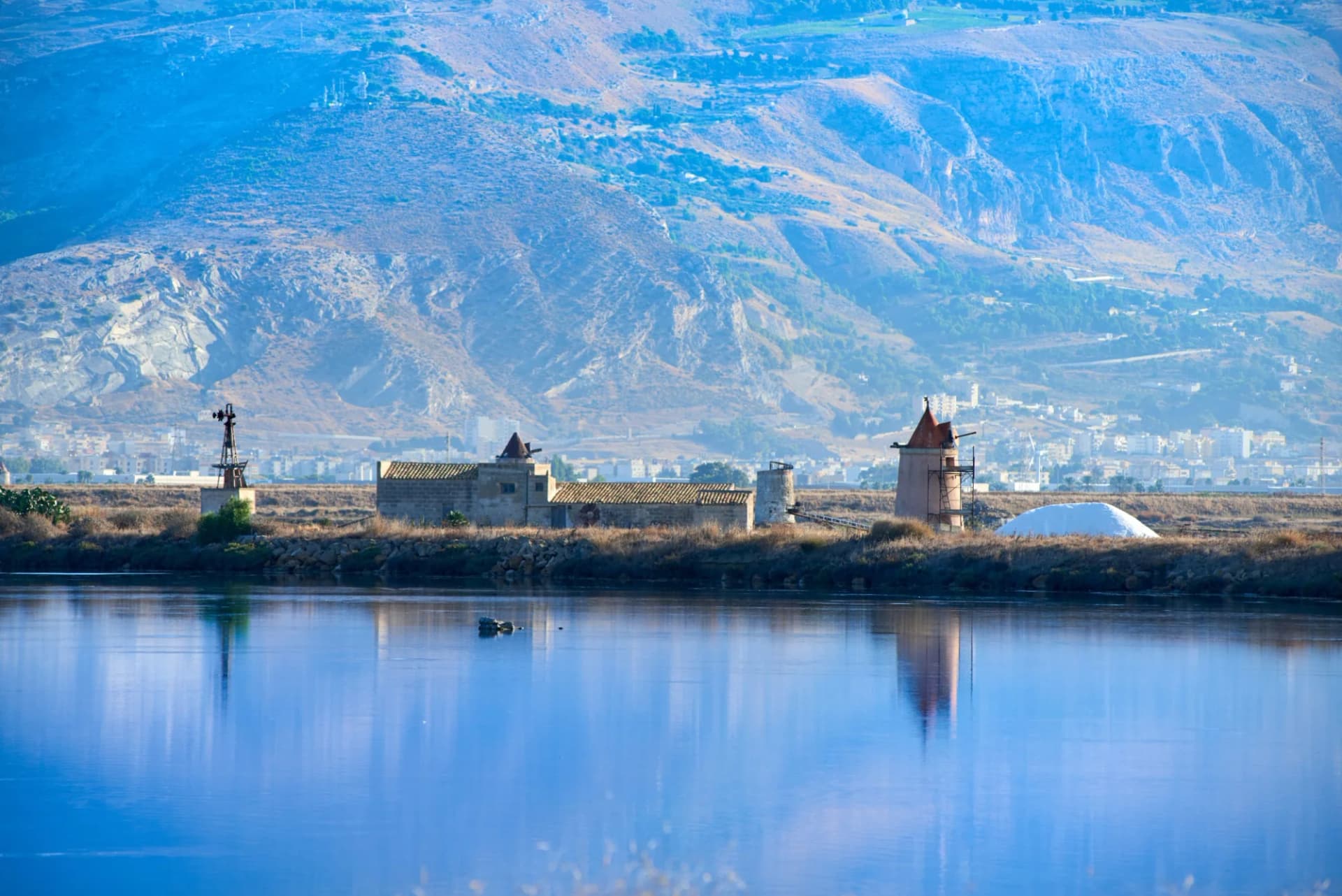 Salt pans with historic buildings and windmills reflected in water, Trapani, Southern Sicily.