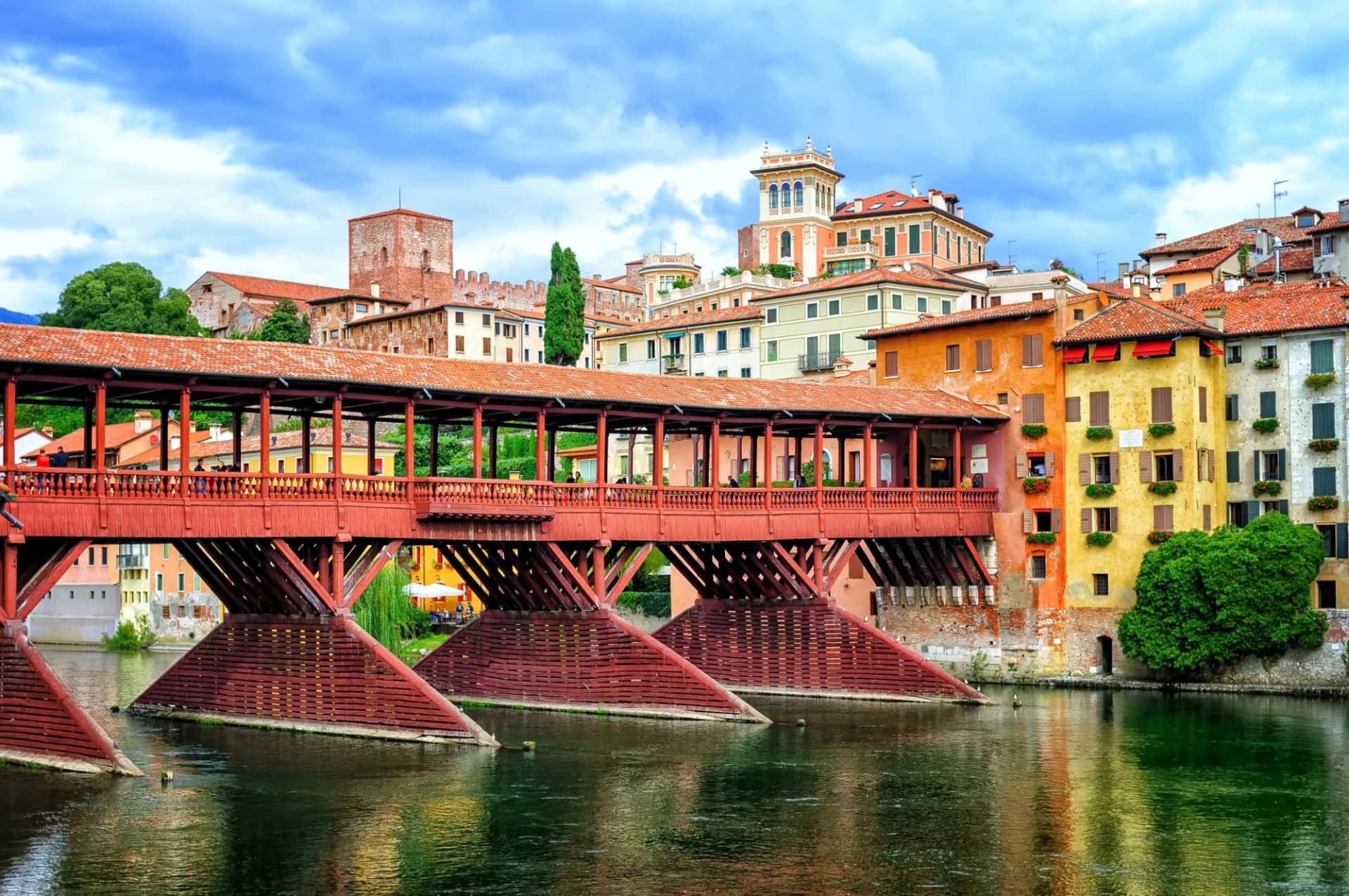 Covered wooden bridge over river in Bassano del Grappa, Italy, with colorful buildings.