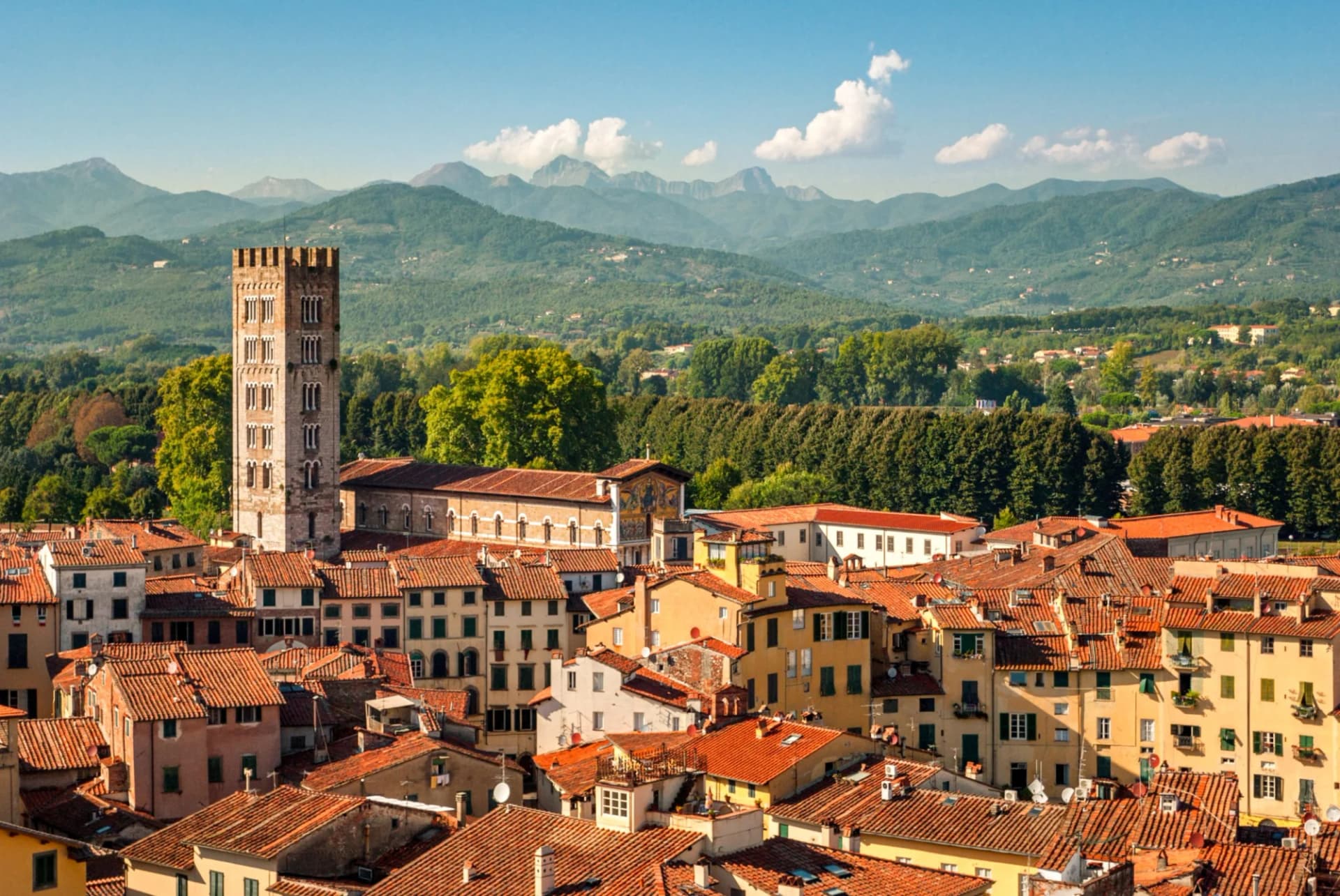 Lucca, Italy panorama with cathedral tower, terracotta roofs, and green mountains.