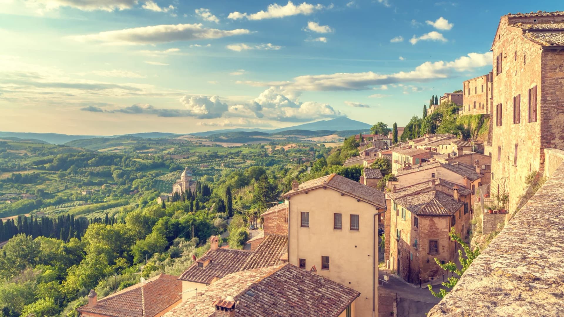 Tuscan landscape and Montepulciano town buildings seen from the walls under a partly cloudy sky.