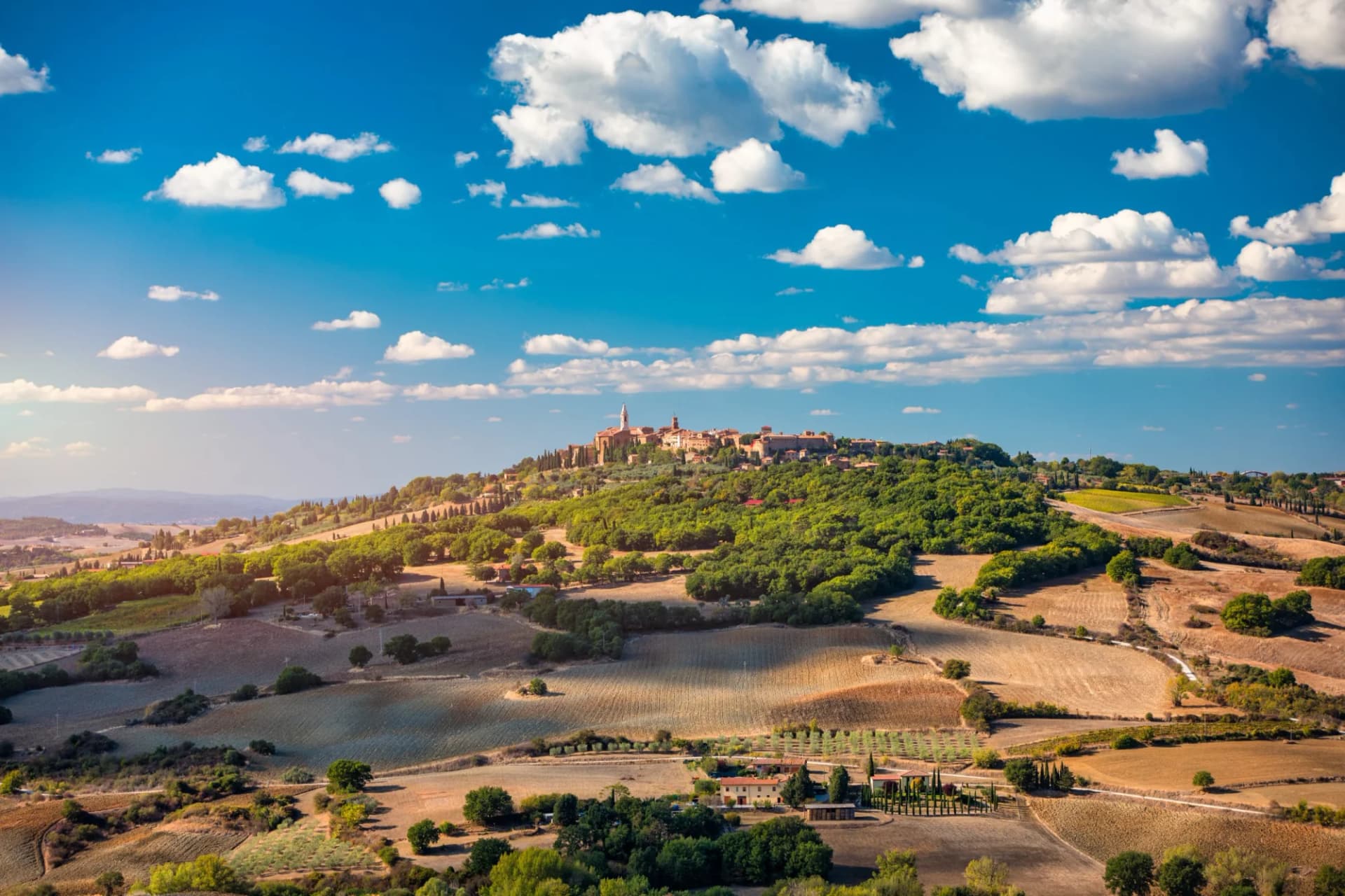 Pienza town on a hilltop overlooking rolling Tuscan fields under a bright blue sky.
