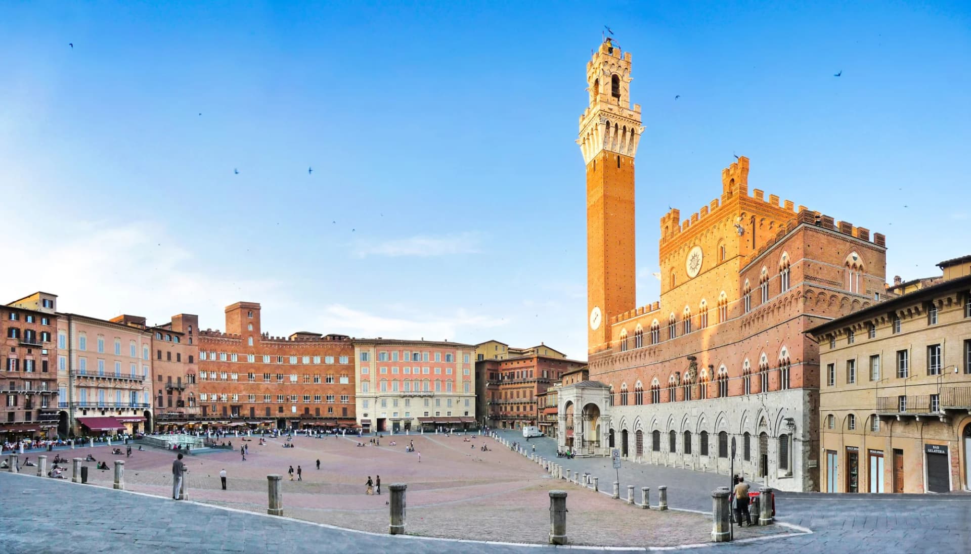 Panoramic view of Piazza del Campo in Siena, Tuscany, with the Palazzo Pubblico tower at sunset.
