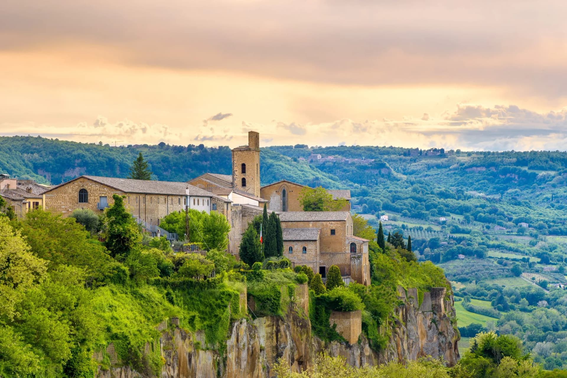 Old town of Orvieto, Italy, perched on a cliff above lush green valleys at sunset.