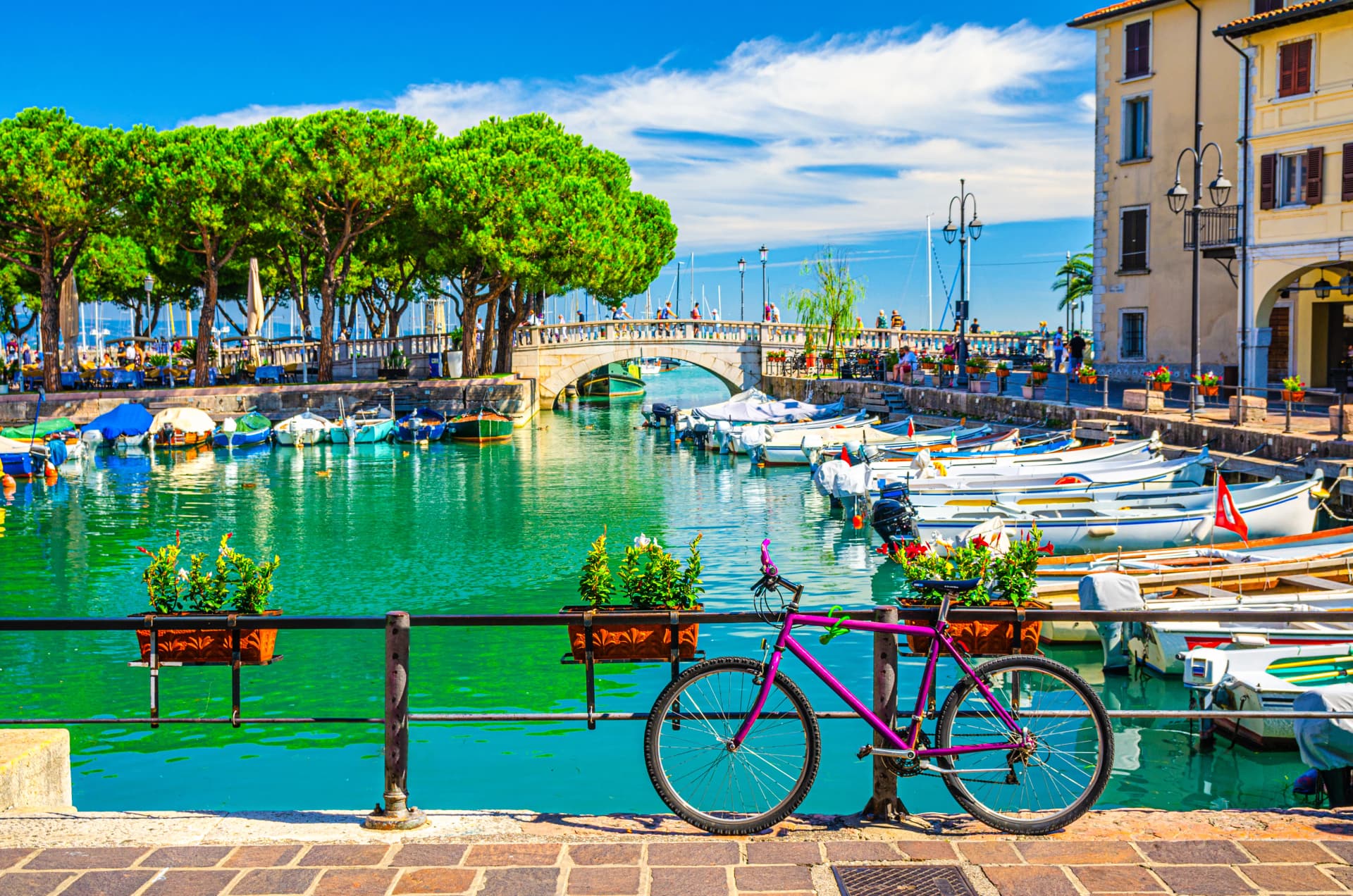 Bicycle bike near fence of old harbour Porto Vecchio with motor boats on turquoise water and Venetian bridge in historical centre of Desenzano del Garda town