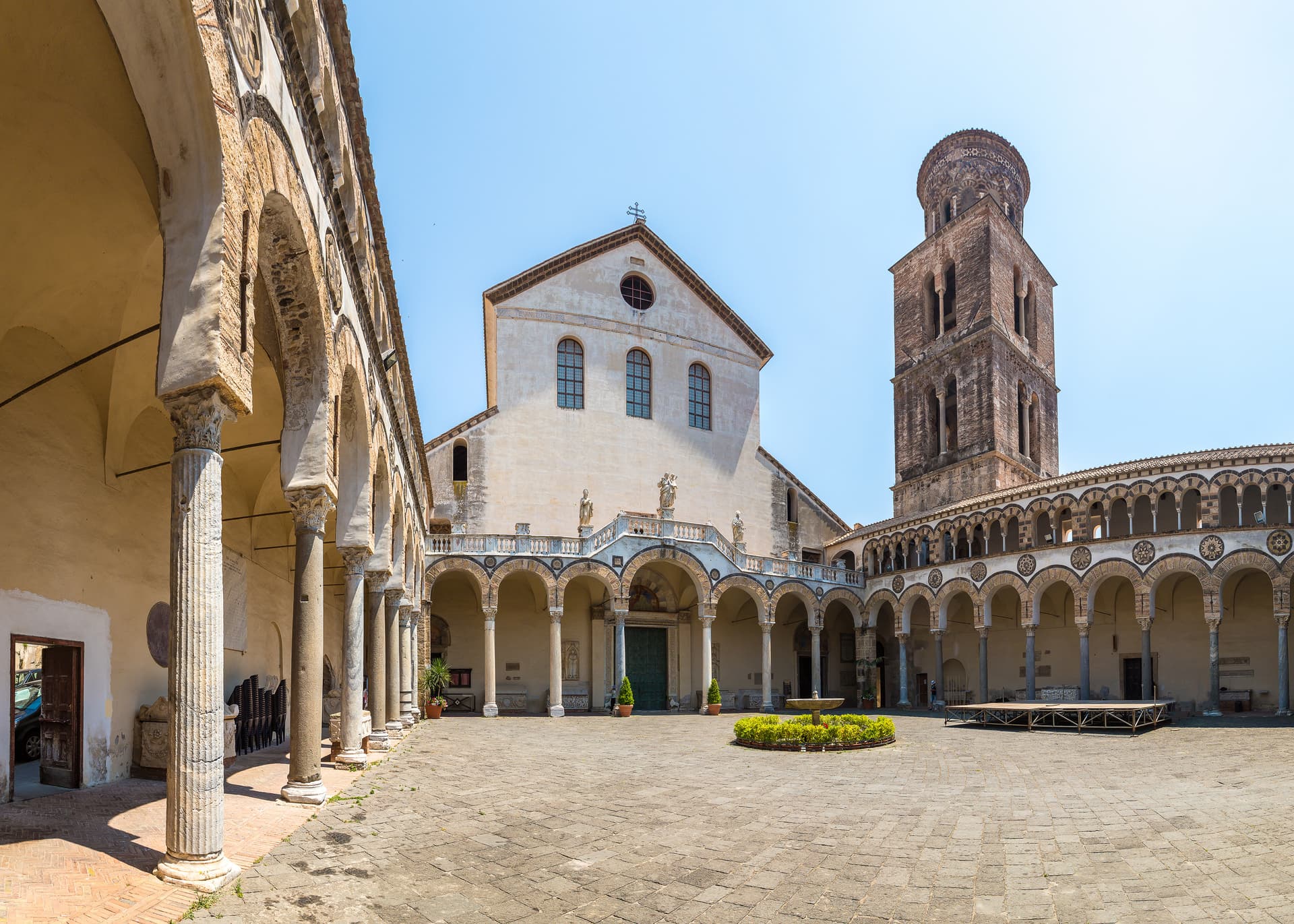 Courtyard of Salerno Cathedral with cloister arches, bell tower, and central fountain under clear sky.