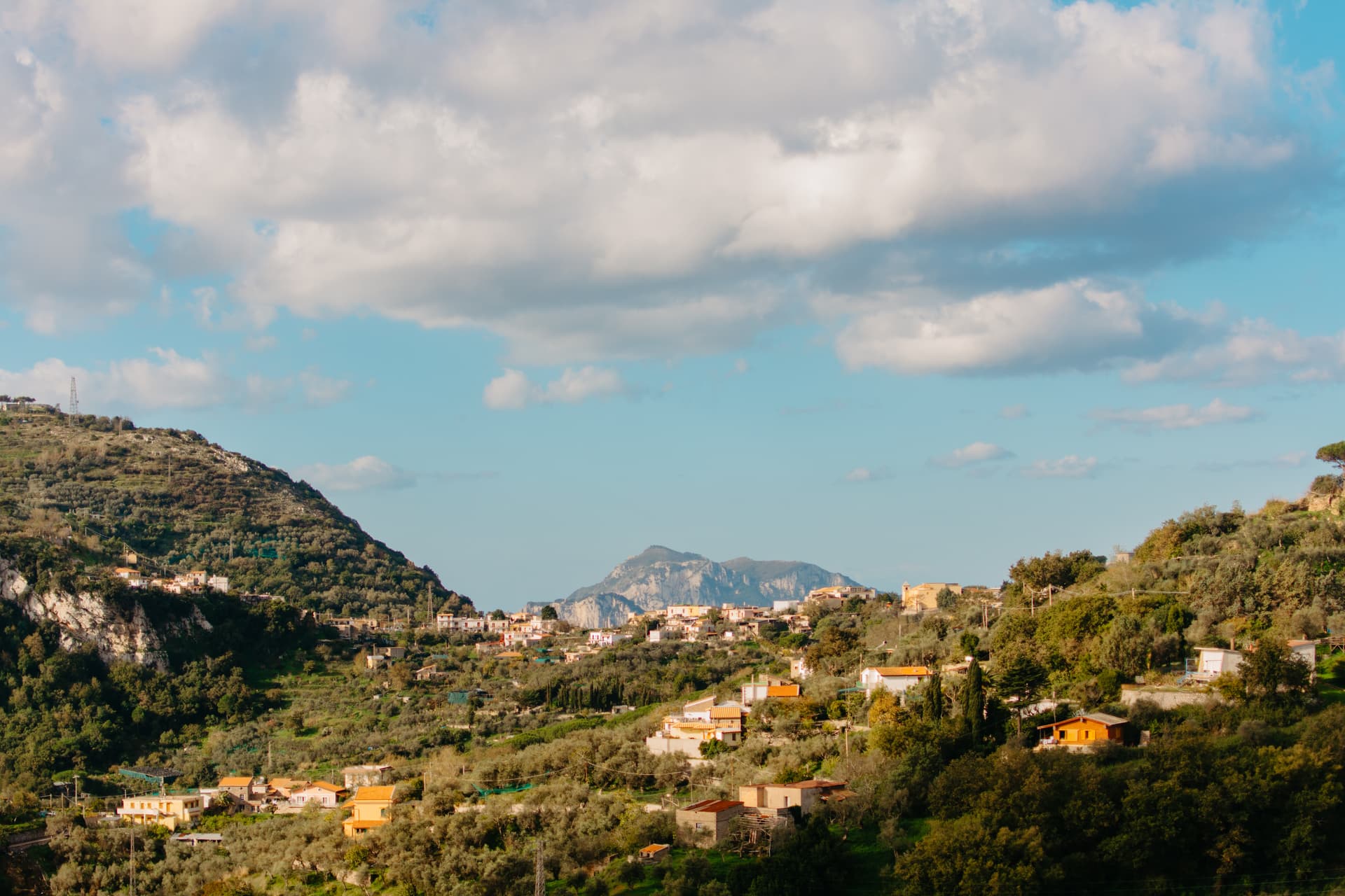 Houses nestled in green, terraced hillsides under a partly cloudy blue sky, Tramonti, Amalfi Coast.