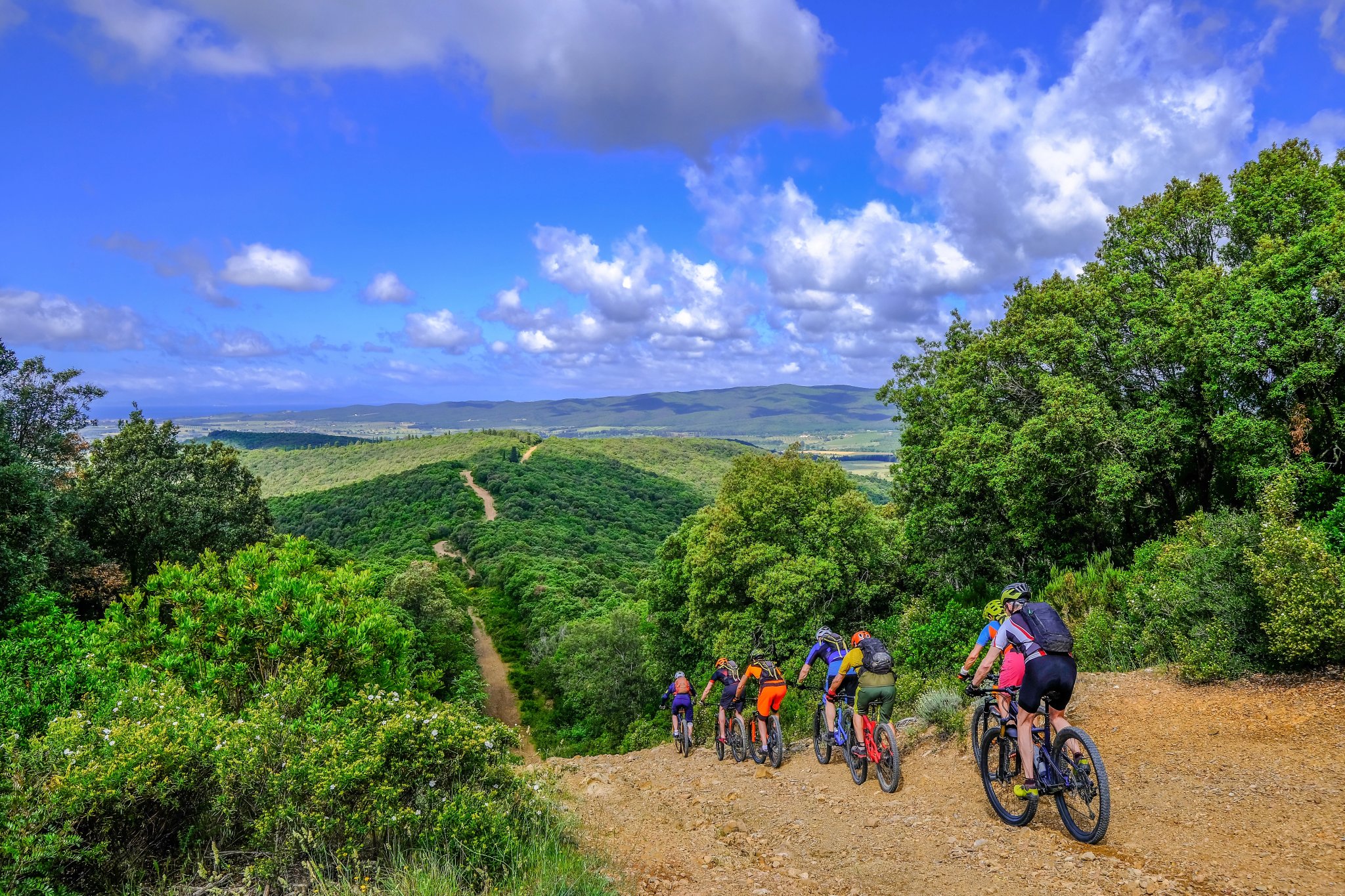 Ugenkendelige mountainbikere cykler på en brandbælte sti over det smukke landskab med sine bakker i Toscana, Massa Marittima, Italien