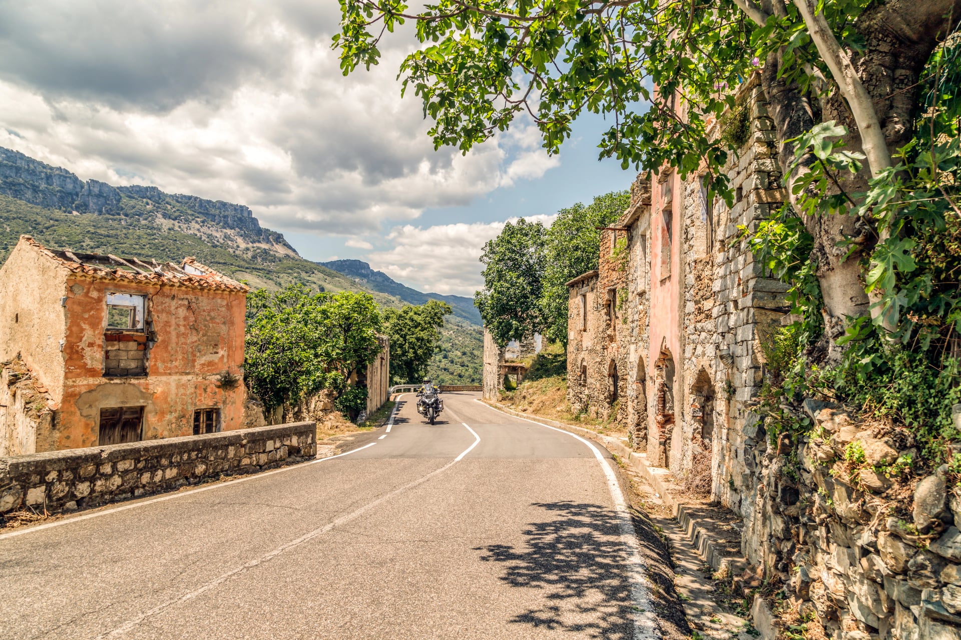 The road in the mountains to abandoned old village Gairo Vecchio, destroyed by a flood and called Ghost Town. Motorcyclist on the road. South Sardinia, Italy.