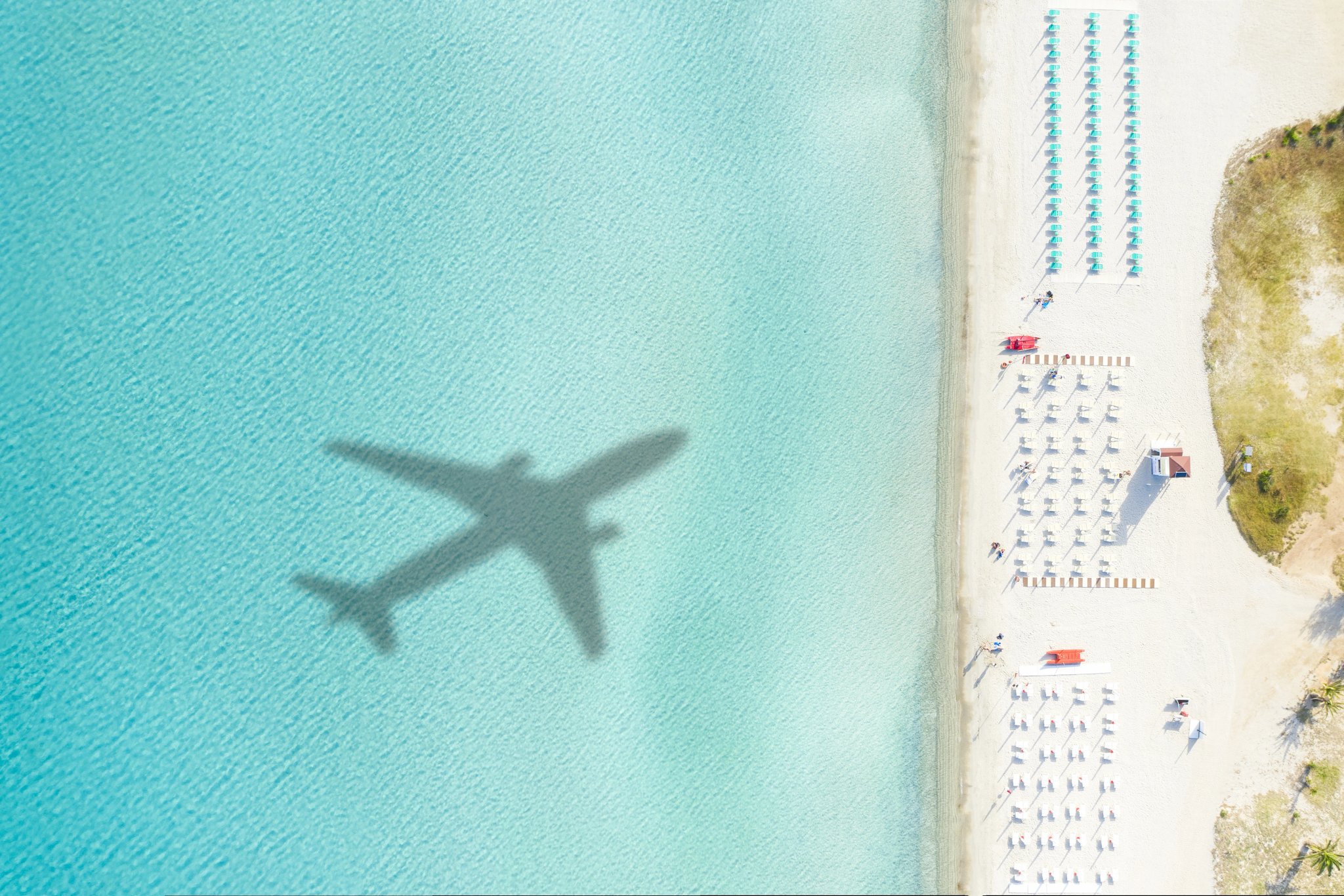 View from above, stunning aerial view of a white sand beach with beach umbrellas and the shadow of an airplane on a beautiful turquoise sea. Porto Rotondo,Sardinia, Italy.