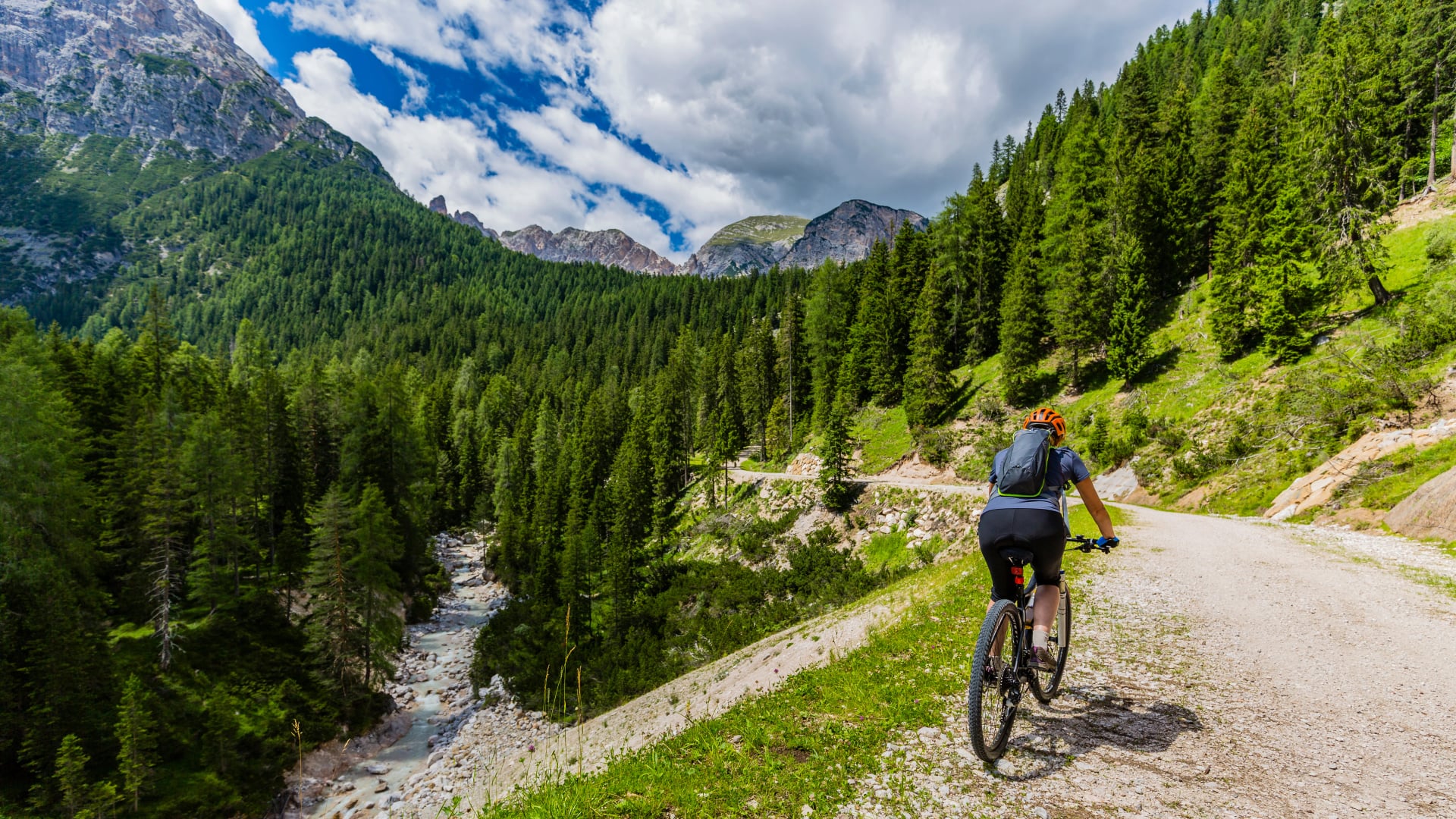 Tourist cycling in Cortina d'Ampezzo, stunning rocky mountains on the background. Woman riding MTB enduro flow trail. South Tyrol province of Italy, Dolomites.
