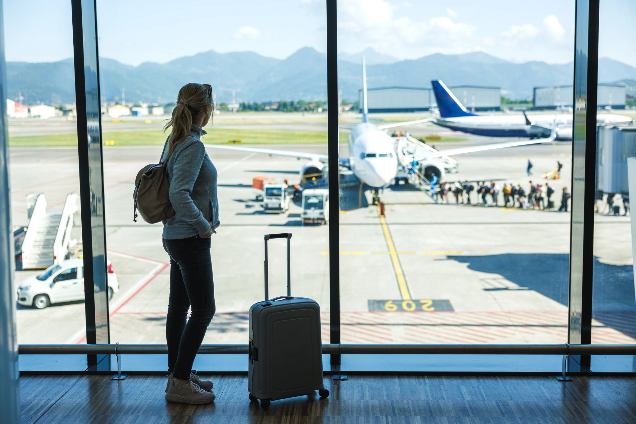 Woman with suitcase waiting at airport terminal before boarding airplane, solo travel passenger ready for flying to summer vacation