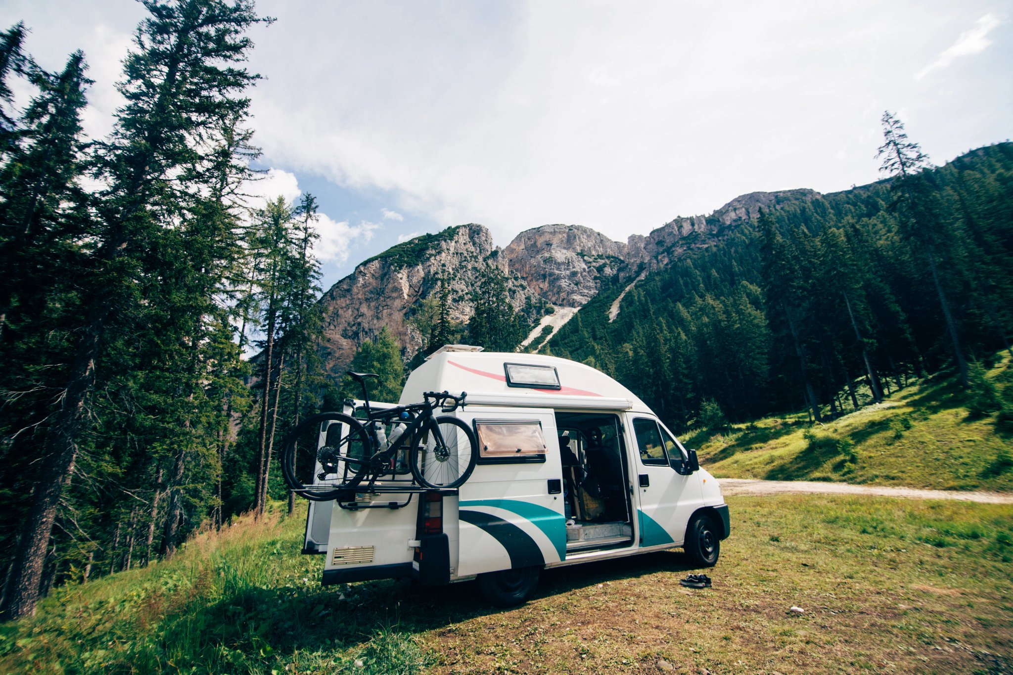 Cute vintage camper van or camping RV parked in wild camping spot in mountain forest. Bicycle on bike rack parked next to converted van. Life on the road in van, outdoor nomadic lifestyle